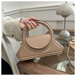 Close-up of model holding a beige geometric leather handbag with a round handle