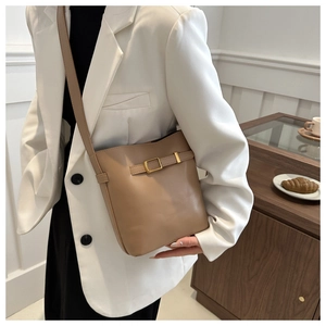 Close-up of khaki bucket bag with gold square buckle worn by a model in a minimal setting