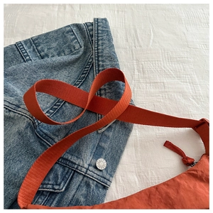 Detail of orange nylon crossbody bag with wide webbing strap and textured fabric