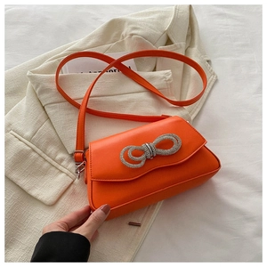 Detailed view of an orange crossbody bag featuring a sparkling silver rhinestone bow