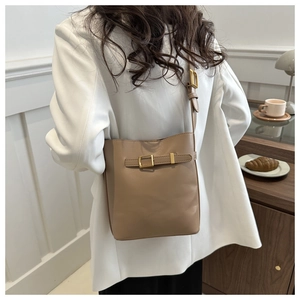 Lifestyle view of a khaki leather bucket bag with gold buckle on a white blazer outfit