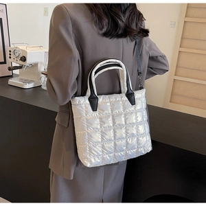 Detailed view of pearl white quilted puffer tote bag on a person in a cozy cafe setting
