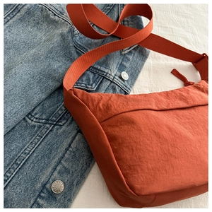 Detail of orange nylon crossbody bag on denim jacket showing fabric texture and strap