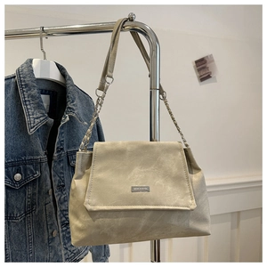 Detail view of beige suede flap bag with metal logo and leather-chain shoulder strap