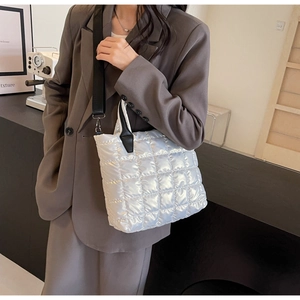 Detail view of a white quilted tote bag with metallic finish and black shoulder strap