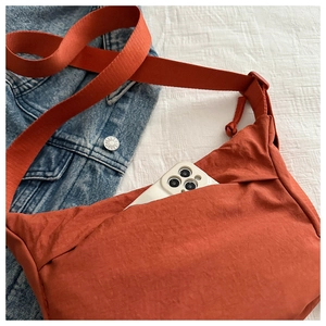 Detail of brick red nylon crossbody bag showing the side pocket and fabric shoulder strap