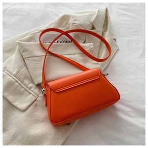 Detail of bright orange PU leather crossbody bag on white blazer with metal hardware