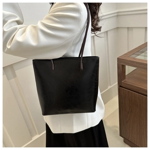 Detail of minimalist black tote bag with polished finish and brown shoulder strap