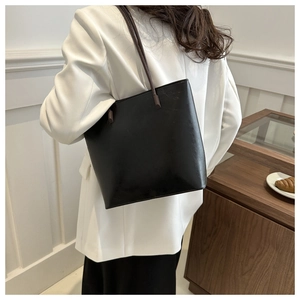 Detail view of the black minimalist bucket bag with dark brown straps worn by a model
