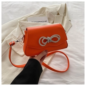 Detail of orange leather crossbody bag with a large silver rhinestone bow ornament