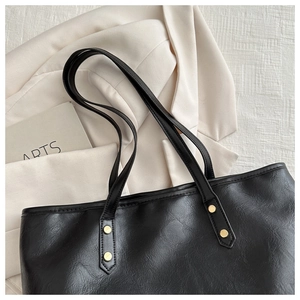 Close-up of black leather tote bag with gold rivets on textured white background