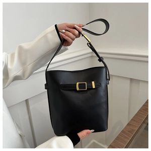 Detail of black PU leather bucket bag with gold buckle held by model in white suit