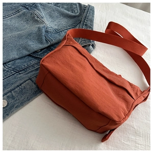 Detail of orange nylon crossbody bag with wide strap on denim jacket background
