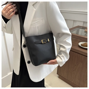 Detail of black matte bucket bag with gold buckle on a model in a white blazer
