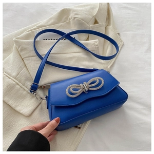 Detail of royal blue square bag featuring a sparkling rhinestone bow and smooth finish