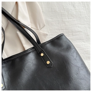 Close-up of black textured leather tote bag showing golden rivet details and retro finish