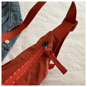 Detail of orange nylon crossbody bag showing pleated texture and adjustable strap
