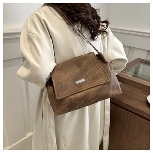 Close-up of a dark brown retro chain bag worn over a cream coat in a stylish setting