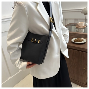 Detail of black matte leather bucket bag with gold hardware worn over a white blazer