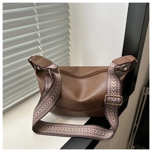Detail of dark brown crescent bag showing pebble leather texture and woven shoulder strap