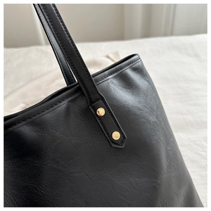 Detail of black faux leather tote bag showing fine texture and gold rivet hardware