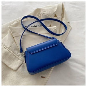 Detail of royal blue leather crossbody bag with silver buckle on neutral fabric