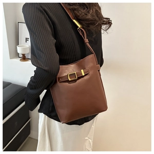 Detail of vintage brown leather bucket bag featuring a decorative gold metal buckle strap