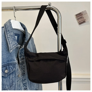 Detail of a black minimalist canvas crossbody bag hanging next to a denim jacket