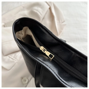 Close-up of smooth black leather tote bag featuring a premium gold metal zipper and beige lining