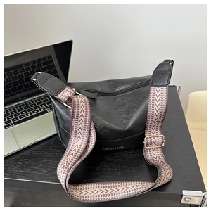 Detail of black lychee texture PU hobo bag with bohemian jacquard strap and gold lettering