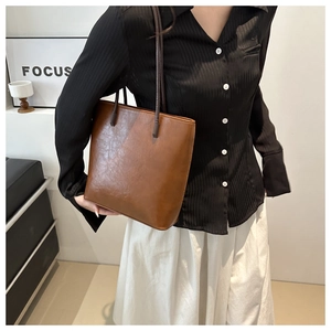 Brown leather tote bag featuring long shoulder straps shown on model for a retro urban look