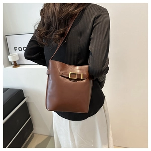Detail of a brown PU leather bucket bag with a golden buckle on a model's shoulder