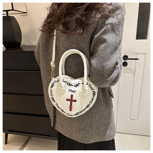 Detail of white heart-shaped handbag with gothic cross print and baby logo text on model
