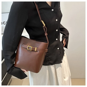 Detail view of deep brown leather bucket bag with gold buckle on casual outfit