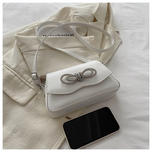 Detail of white leather shoulder bag featuring a sparkling rhinestone bow buckle