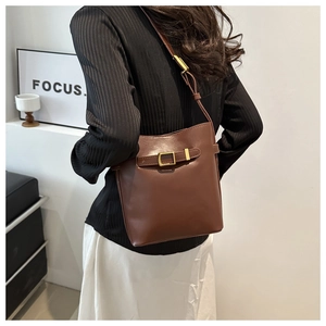 Brown leather bucket bag with gold buckle shown on a model in a minimalist room