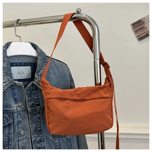 Detail of orange nylon tote bag with wide strap hanging next to a denim jacket