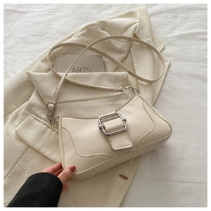 Vue détaillée du sac baguette en cuir crème avec boucle argentée sur tissu texturé