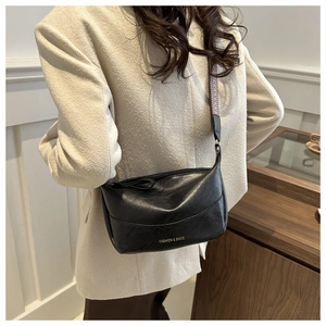 Detail of black faux leather crescent bag with white geometric patterned wide shoulder strap