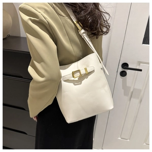 Detail of white bucket bag featuring smooth leather finish and golden metal buckle accents