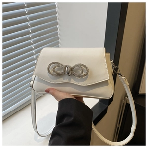 Detail of white leather crossbody bag featuring a rhinestone bow buckle and long strap