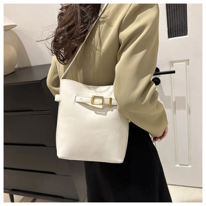 Minimalist white bucket bag with gold buckle detail shown on model in a modern room