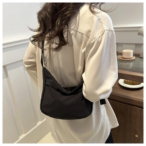 Detail of a minimalist black canvas crossbody bag shown from a back-wearing perspective