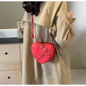 Détail du sac à bandoulière rouge en forme de cœur avec clous sur un trench-coat kaki