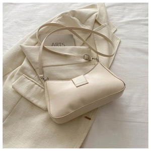 Détail d'un sac baguette en cuir beige crème posé sur une veste de tailleur