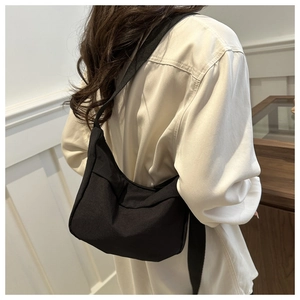 Detail of a large black canvas crossbody tote bag on a model in a minimalist setting