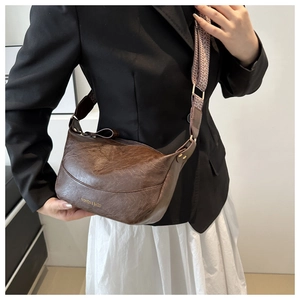 Detail of dark brown vintage texture bag with patterned wide strap and gold hardware