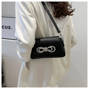 Side view of black matte leather shoulder bag with rhinestone bow on silk blazer