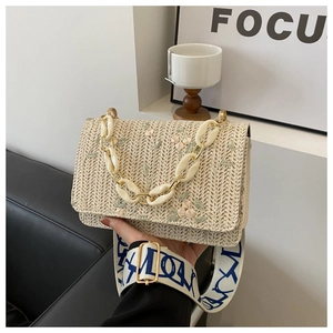 Détail du sac en paille tissée avec broderie florale et bandoulière à texte bleu