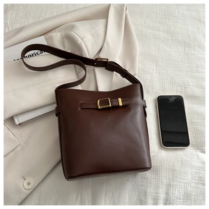 Detail view of deep brown bucket bag with gold buckle and a phone for size scale